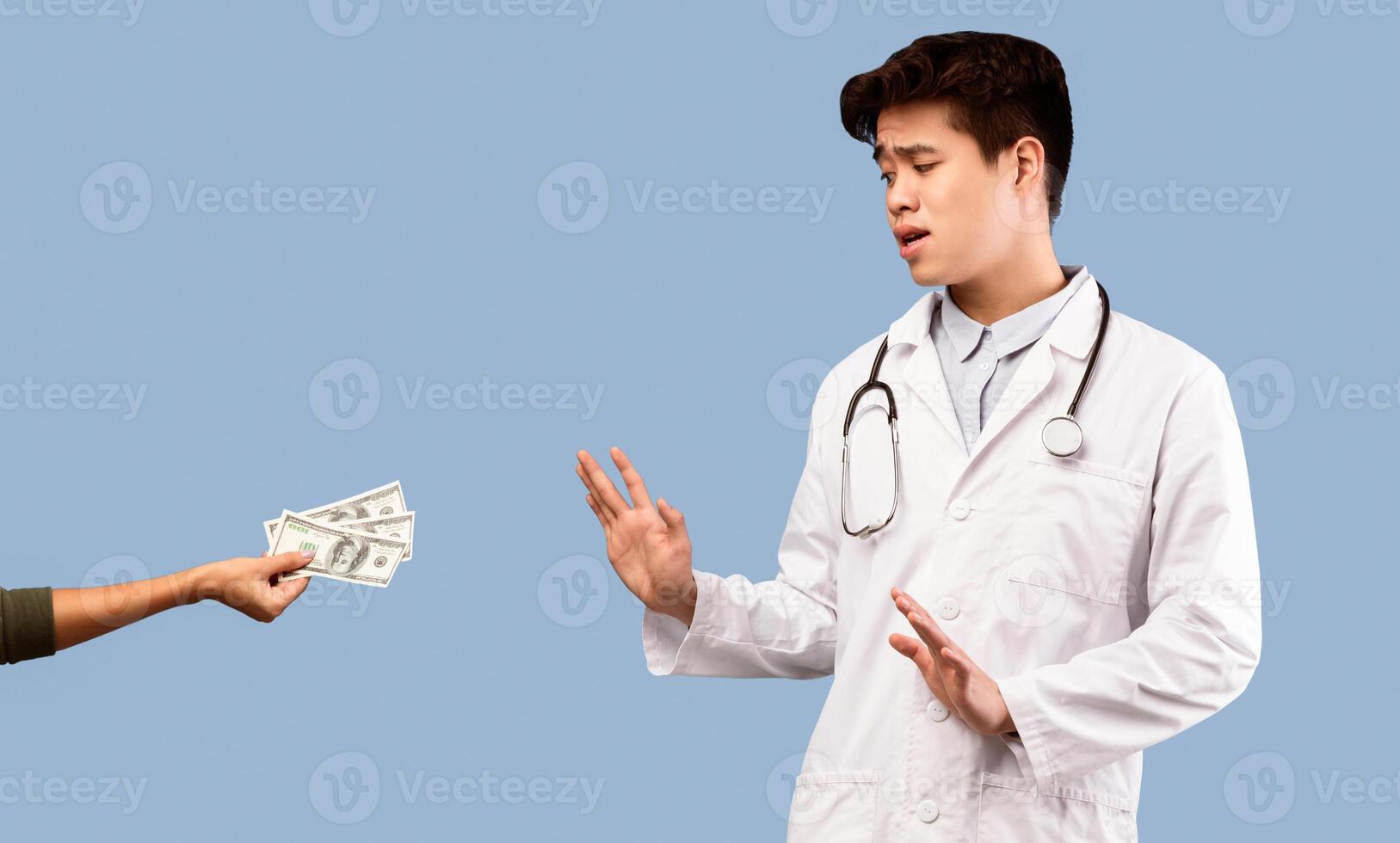 Say No To Corruption Concept. Serious scared asian male doctor in white coat refusing to take bribe from female patient giving him money isolated over studio background, panorama photo