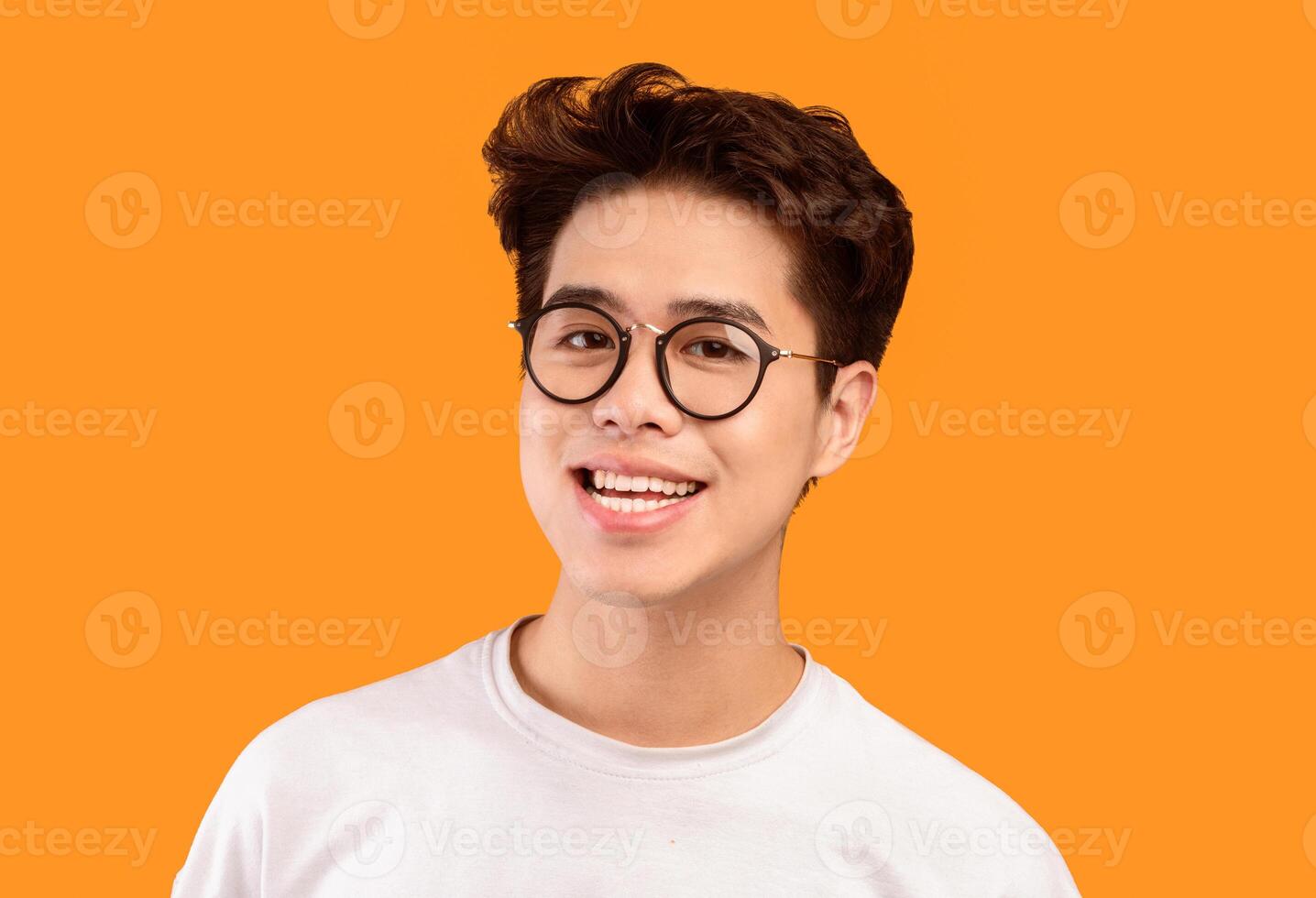 Close up Headshot Portrait Of Smiling Young Asian Man Wearing Stylish Eyeglasses, Looking at the Camera Against Orange Studio Wall Background with Copy Space, Isolated. Happy Guy Posing In Specs photo