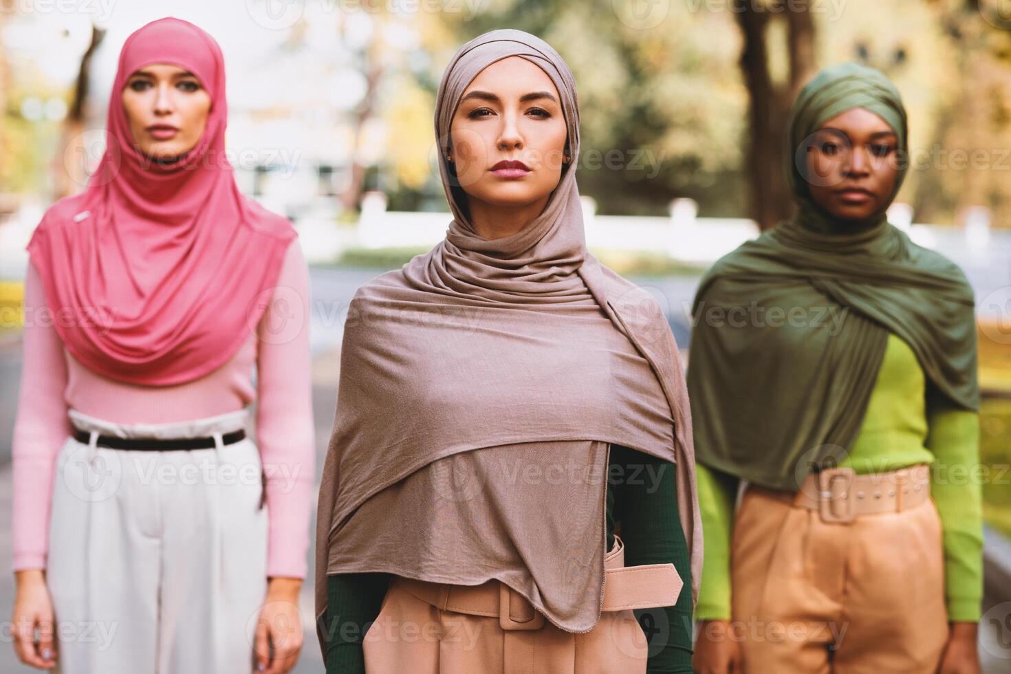 Serious Arab Female Standing In Front Of Diverse Ladies Looking At Camera Outside In City Park. Islamic Women In Hijab Headscarf Posing Together. Selective Focus photo
