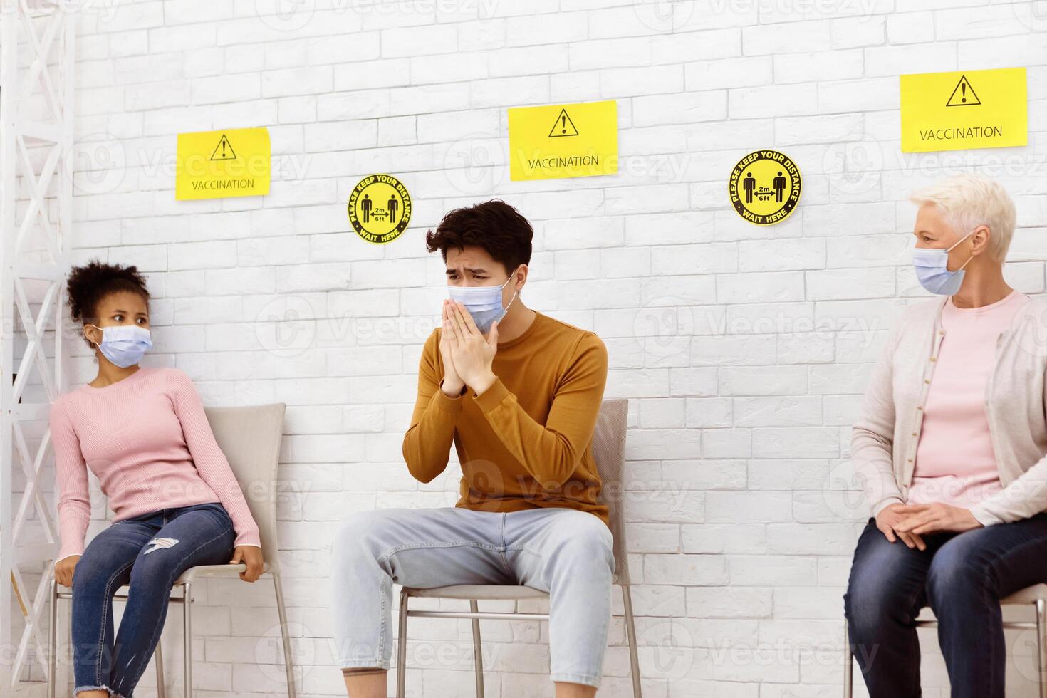 Covid-19, Coronavirus Concept. Chinese Man With Pneumonia Coughing Sitting In Queue With Scared Patients Waiting For Doctor's Appointment In Hospital Waiting-Room. Corona Virus Pandemic Outbreak photo