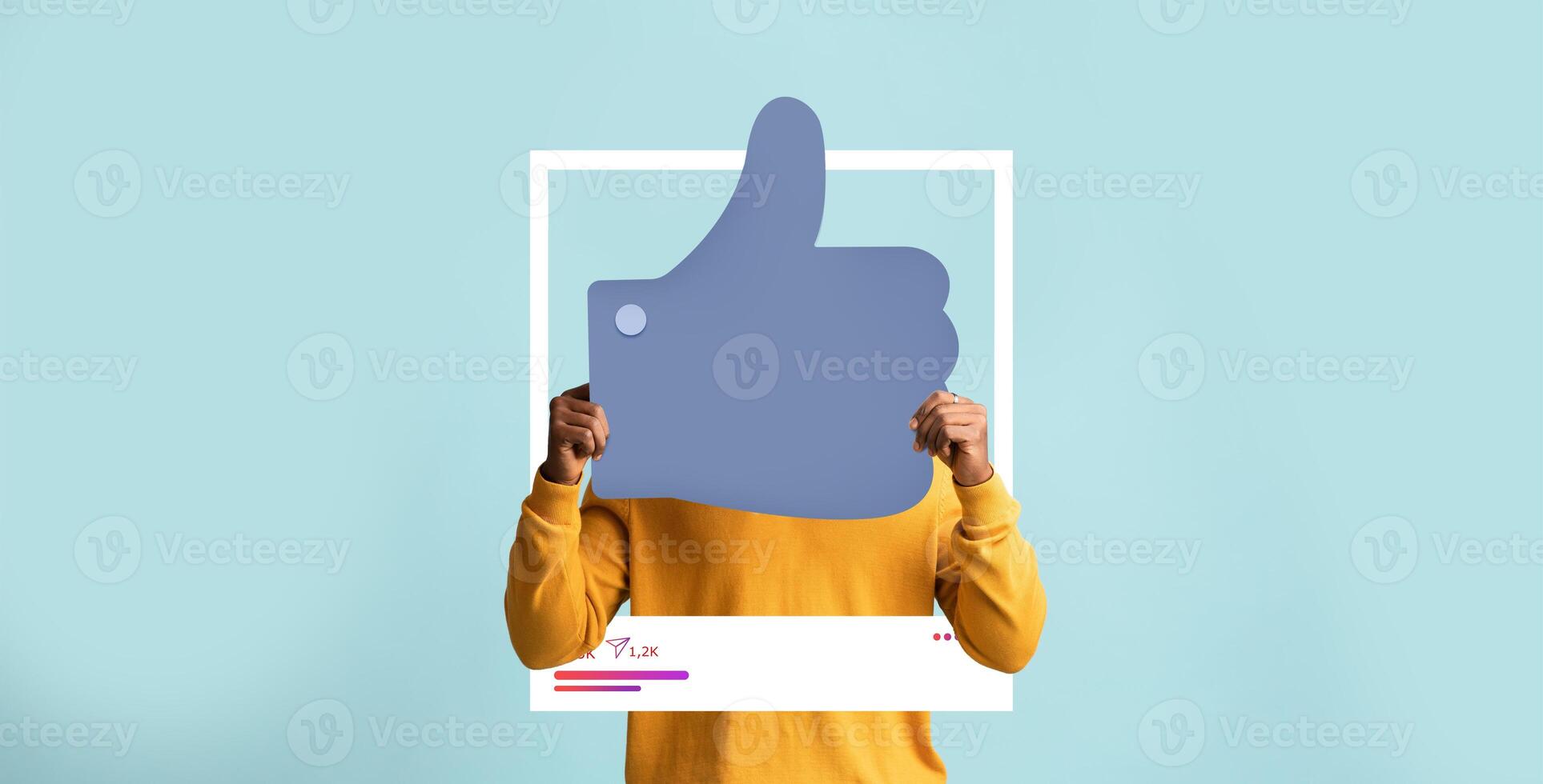 A person wearing a yellow sweatshirt holds a large thumbs-up icon against a light blue background. They celebrate positive engagement on social media platforms as an influencer. photo