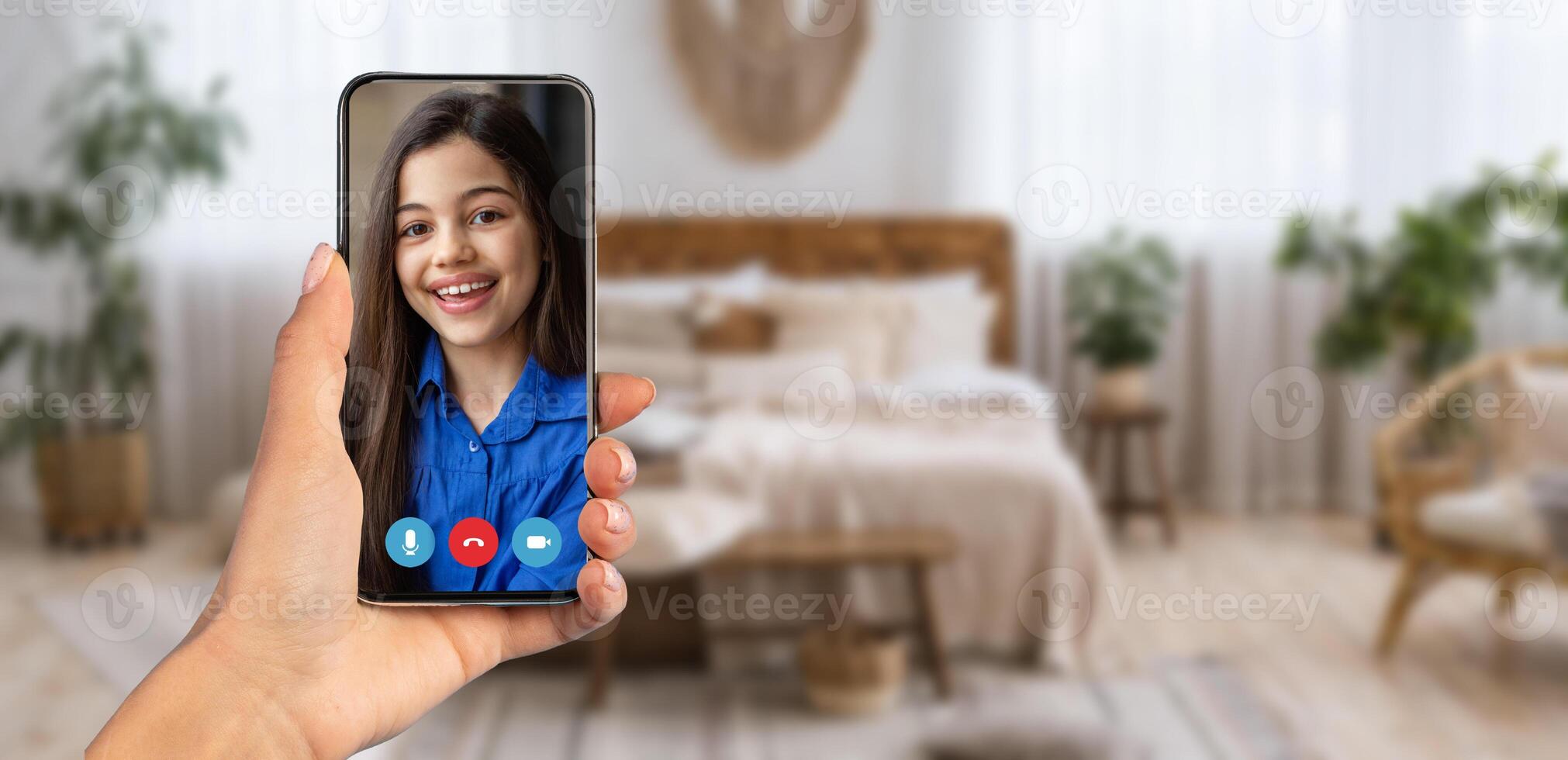 A person is holding a smartphone showing a smiling child on a call. The background is a cozy, bright room that enhances the feeling of connection and interaction. photo