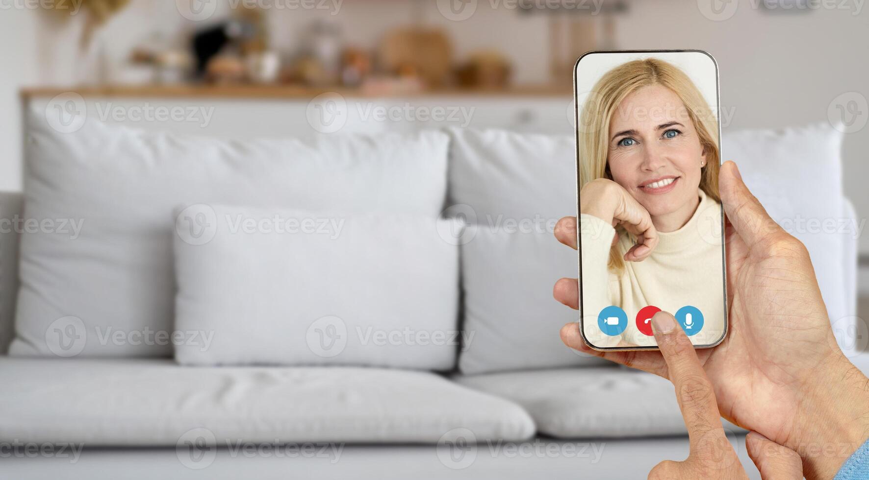 A person is having an online call at home, communicating through a smartphone with smiling senior woman. The relaxed setting is enhanced by a comfy couch in the background. photo