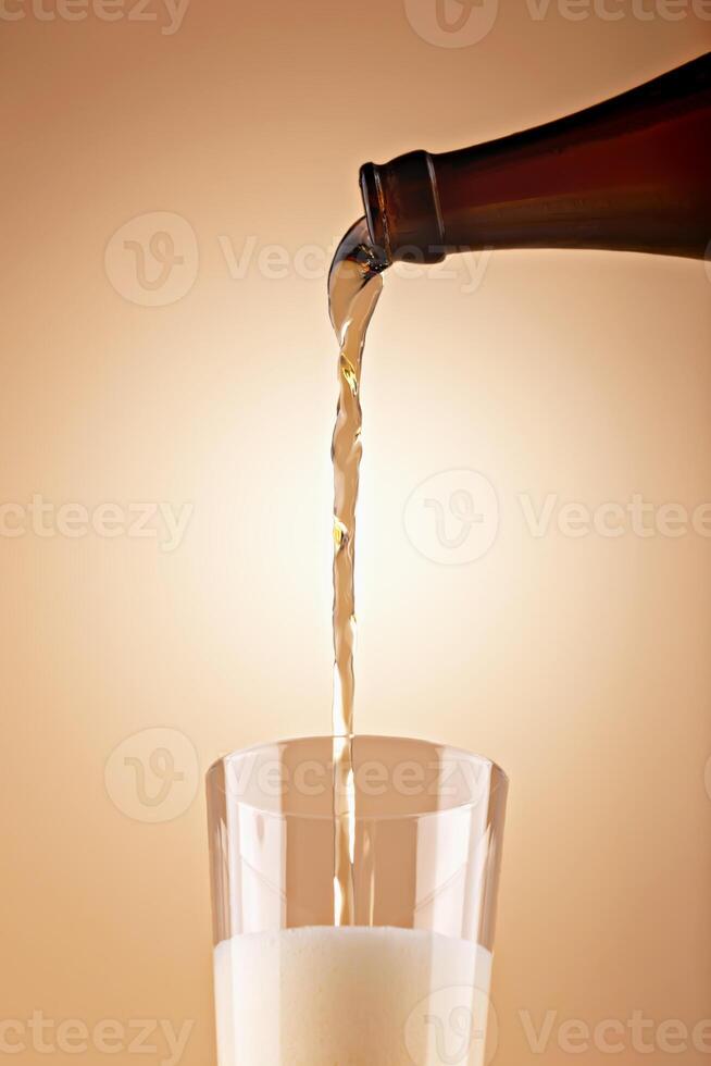 Beer being poured from dark bottle into clear glass with thick foam against warm gradient background photo