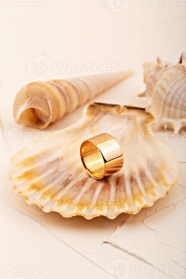 Minimalist gold ring on scallop shell with seashells in background on soft beige surface photo