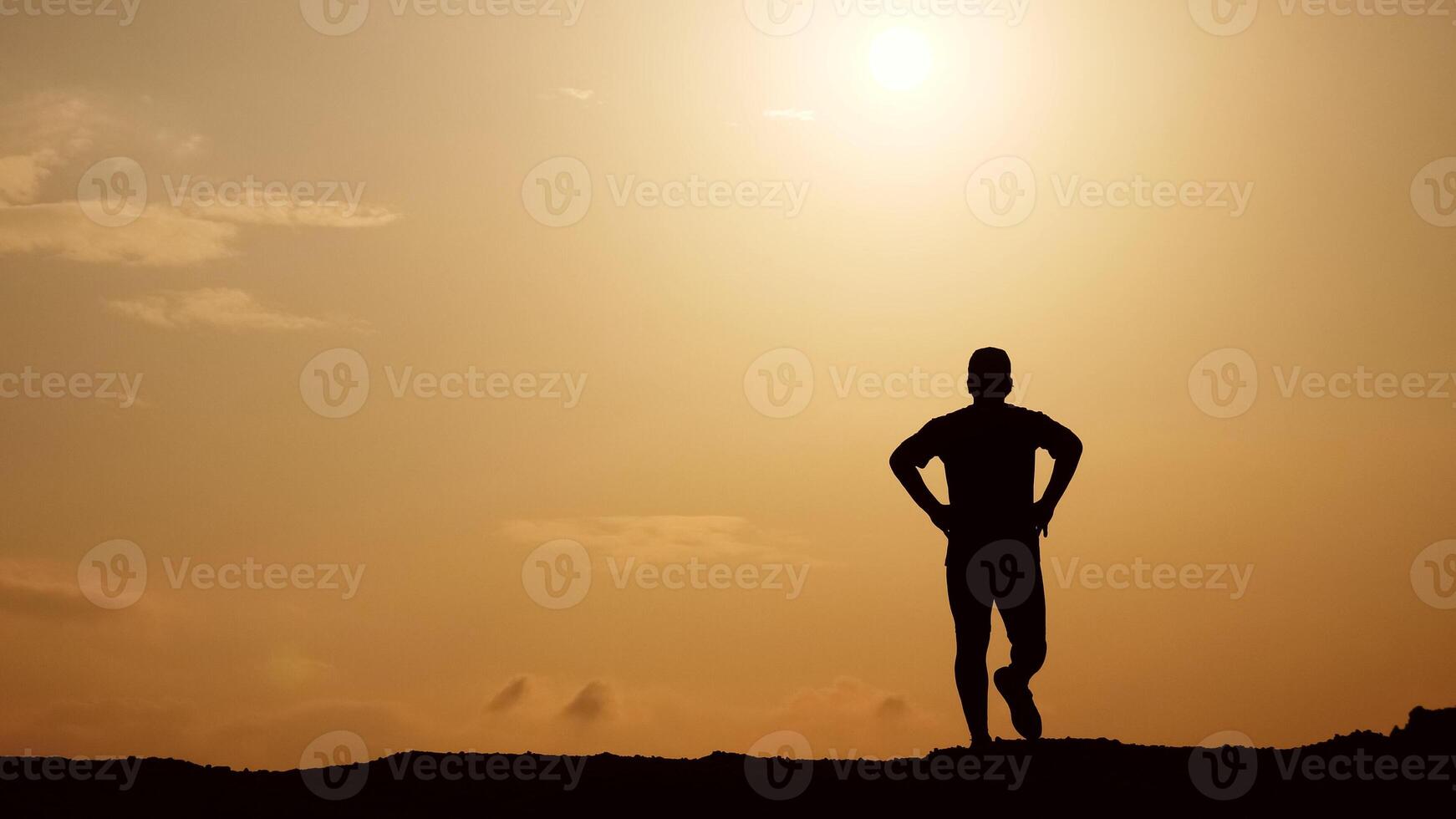 Silhouette of a Person Standing on a Hilltop Against a Golden Sunset Sky with Clouds photo