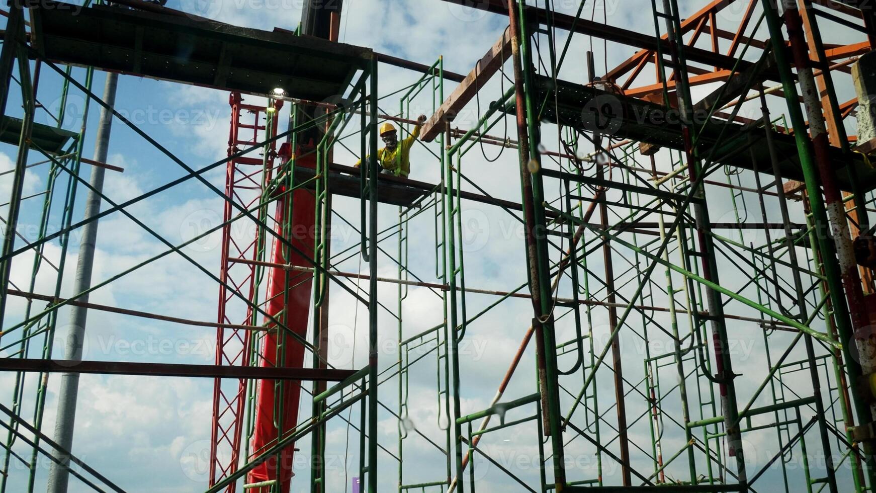 Construction Worker on Scaffolding Against Blue Sky at Building Site with Metal Framework and Safety Gear photo