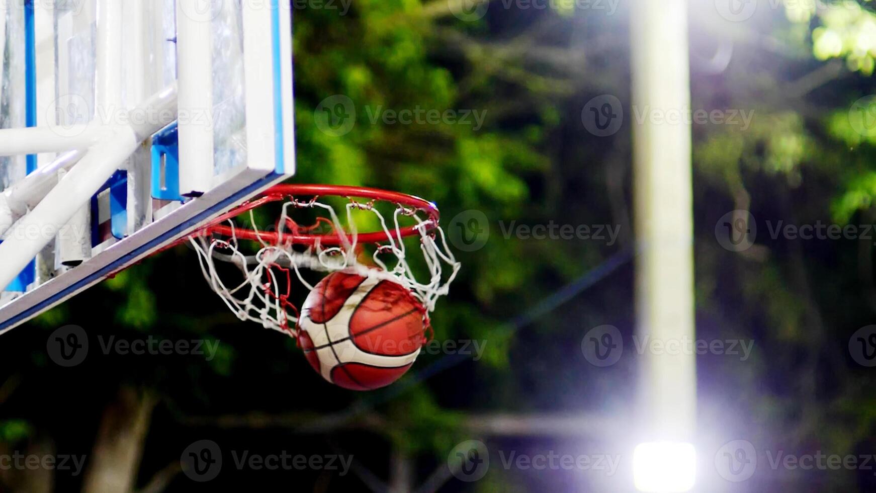 Dynamic Basketball Shot Mid-Air with Hoop and Net in Focus, Capturing the Excitement of Outdoor Sports at Night photo