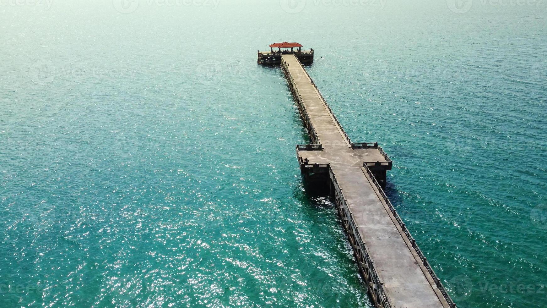 Aerial View of a Long Wooden Pier Extending into the Turquoise Ocean on a Sunny Day with Clear Blue Skies photo