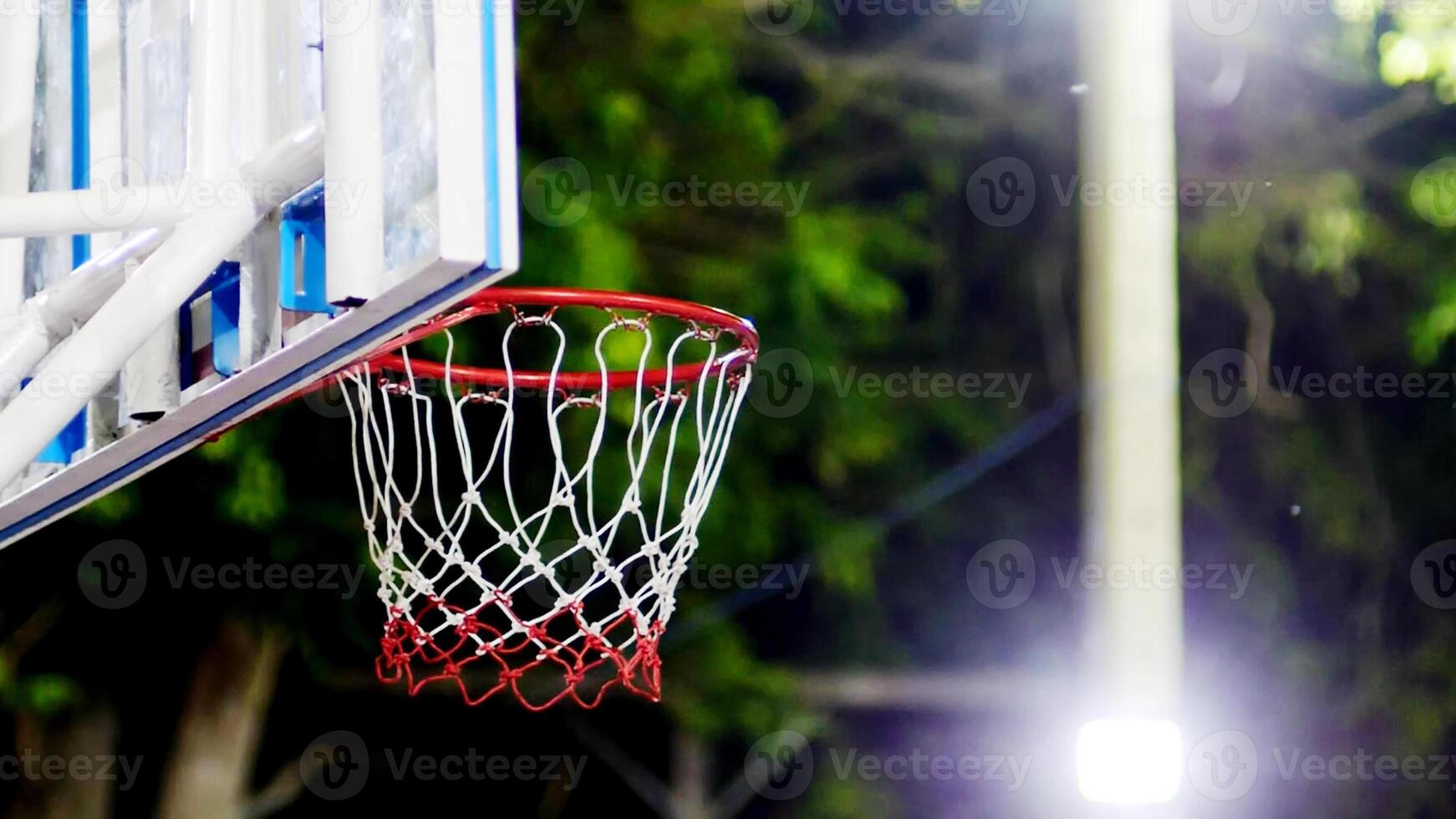 Close-Up of Outdoor Basketball Hoop with Red Rim and Net Under Bright Stadium Lights at Night photo