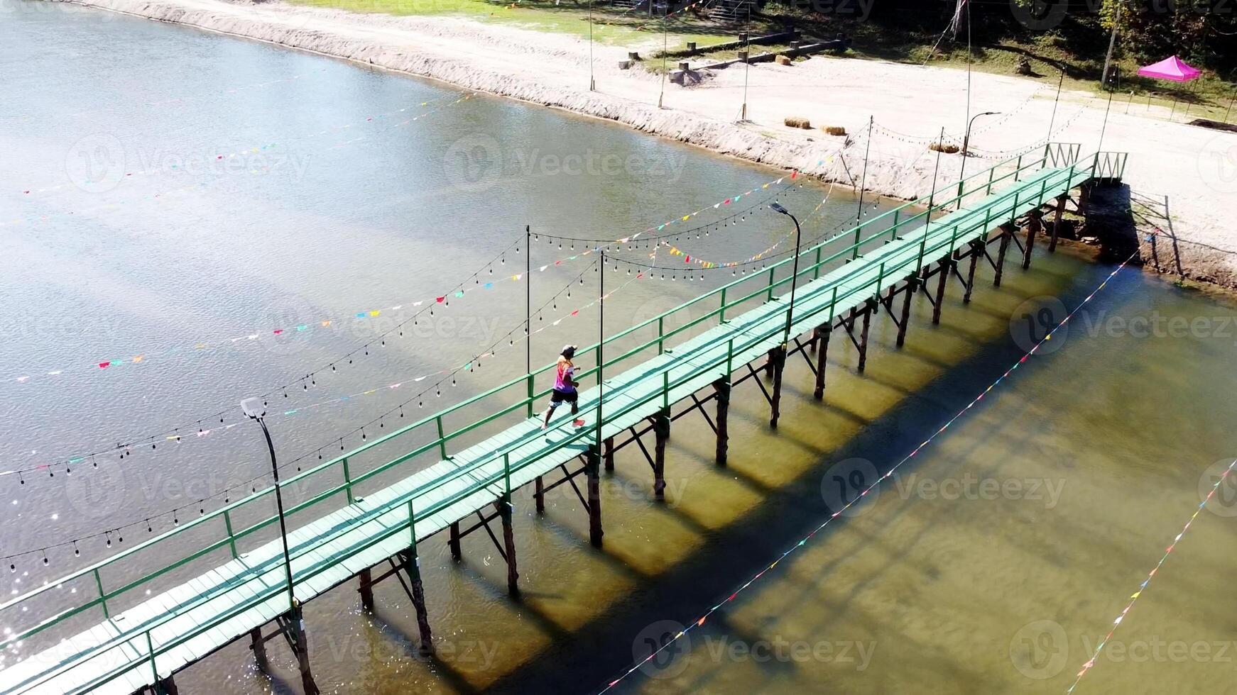 Aerial View of a Vibrant Green Bridge Over Serene Waters with Colorful Decorations and a Lone Walker photo