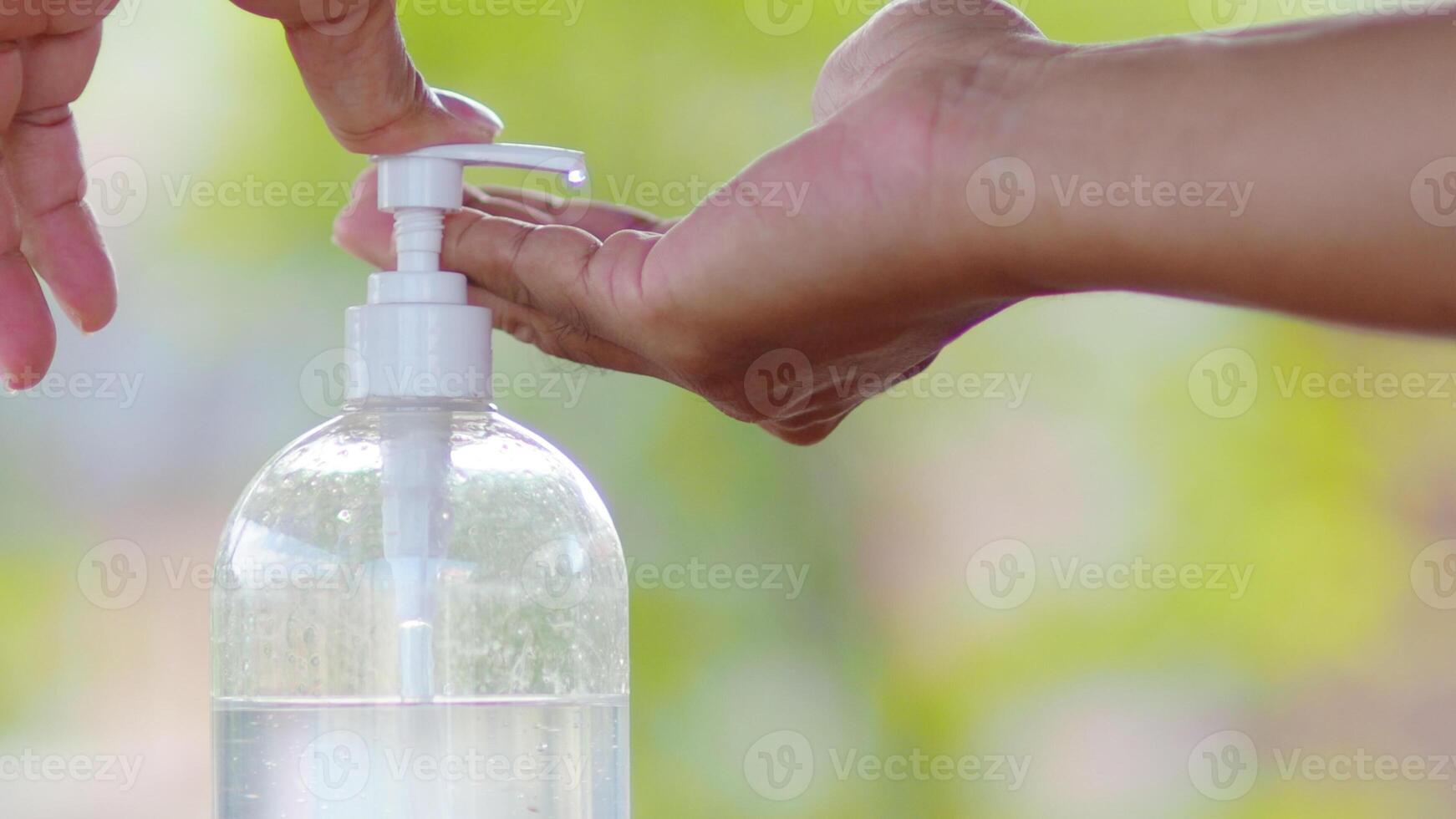 Close-Up of Hands Using Hand Sanitizer Dispenser Outdoors with Green Background photo