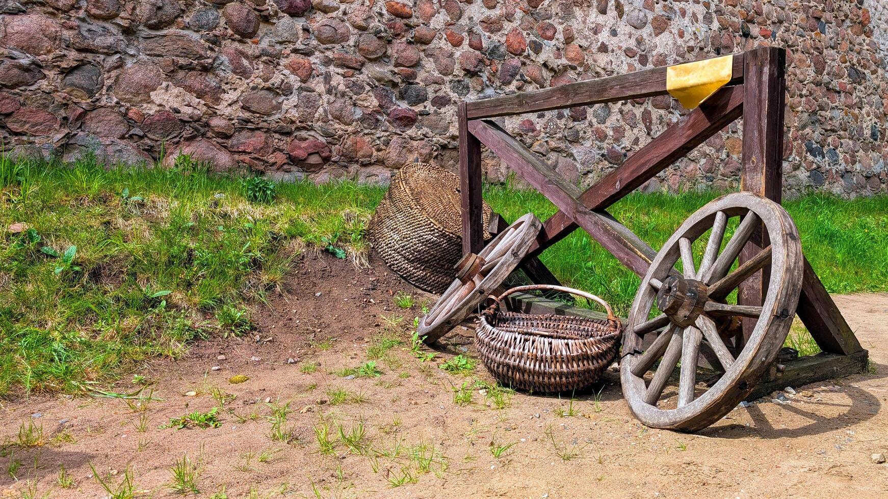 Old wooden cart wheels and wicker baskets near a stone wall in a rustic countryside setting photo