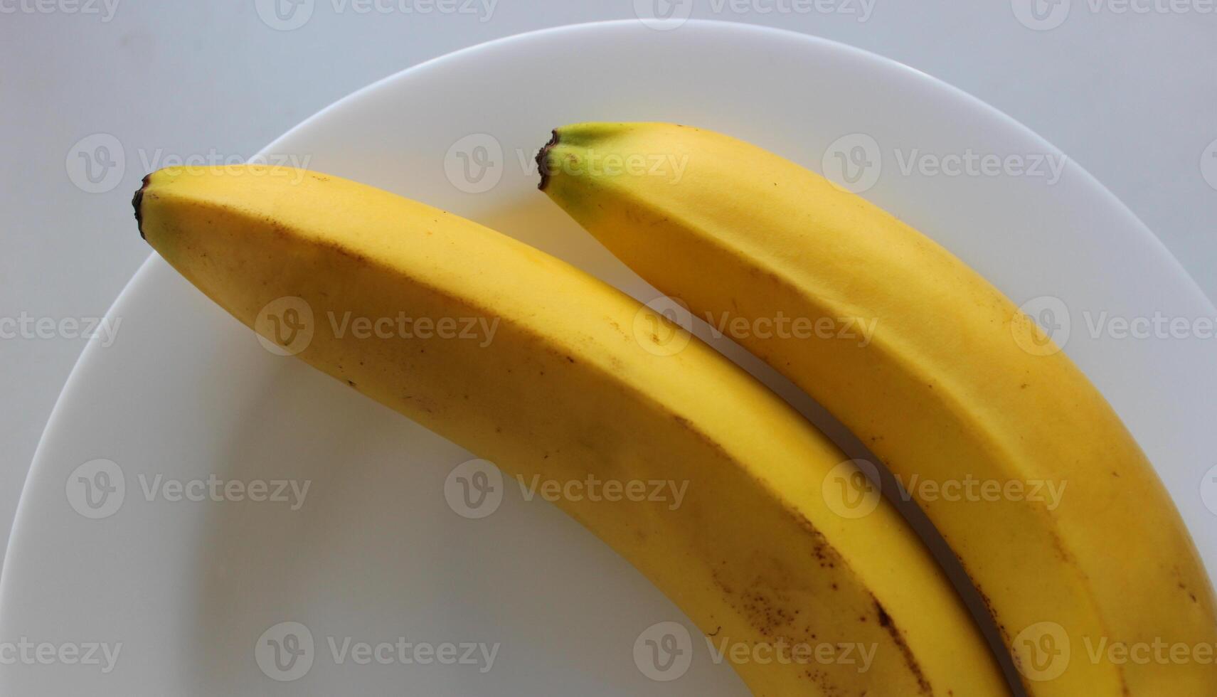 Two whole bananas on white plate closeup view stock photo