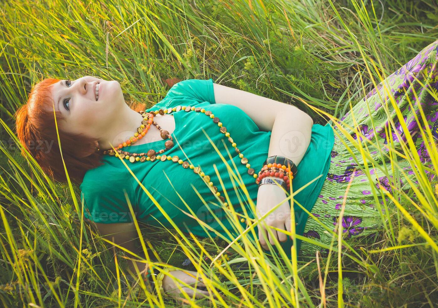Young red-haired woman lying in the grass and enjoying sunny summer day. Happy smiling young girl in nature. photo