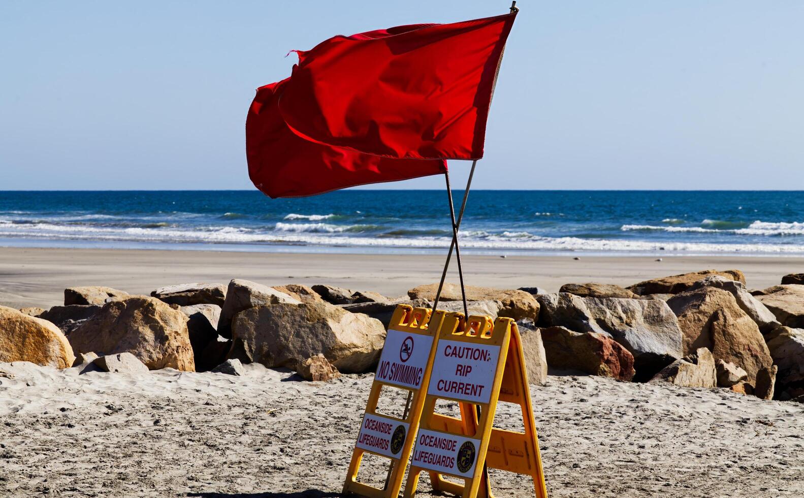 Oceanside, CA, 2024 - Two Red Flags Flying On No Swimming Sign photo