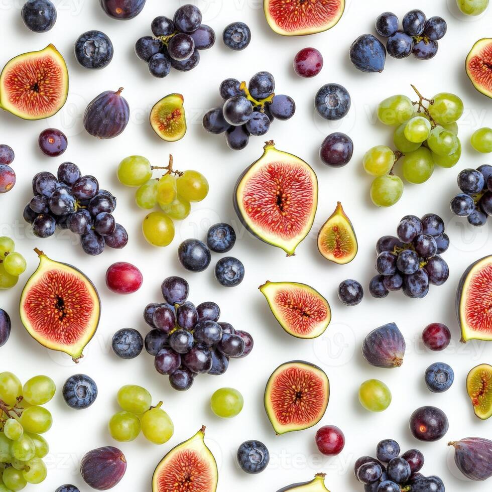 Flat lay of various fresh fruits including figs, green and purple grapes, and blueberries scattered on a clean white surface, creating a colorful and healthy food pattern photo