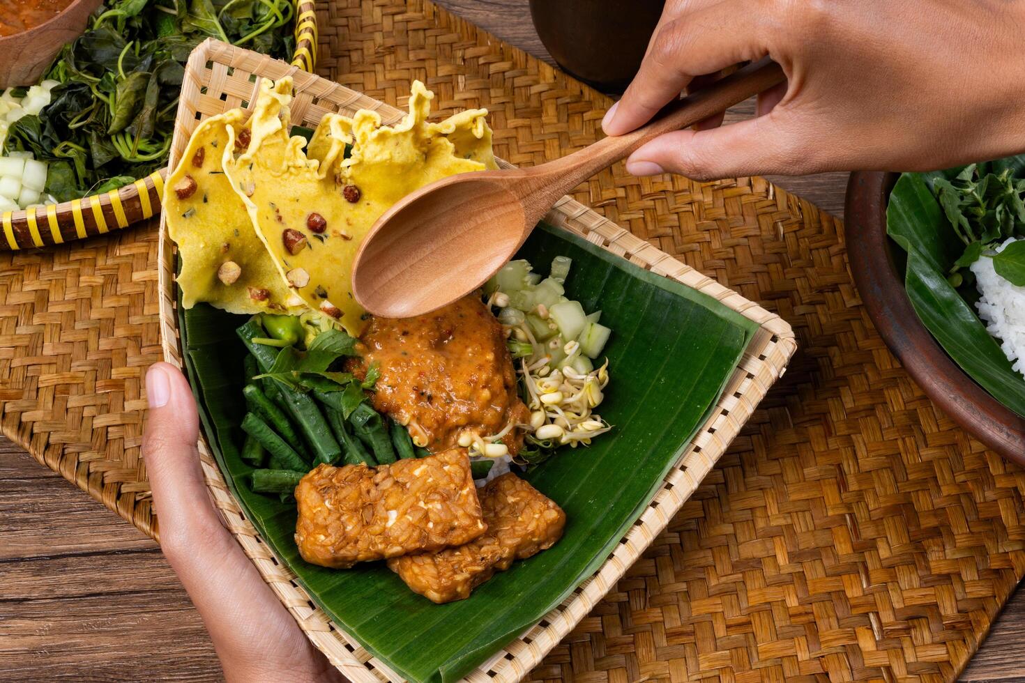 Hand Reaching to Scoop Pecel in Triangular Bamboo Plate photo