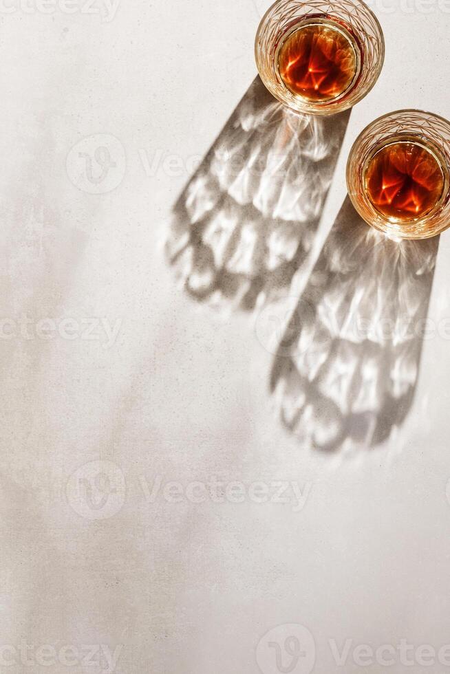 alcohol Glasses with dark shadows at sunlight on beige table, top view minimal lifestyle, aesthetic flat lay shiny glass sparkling at sun, summer strong drink, copyspace, vertical photo