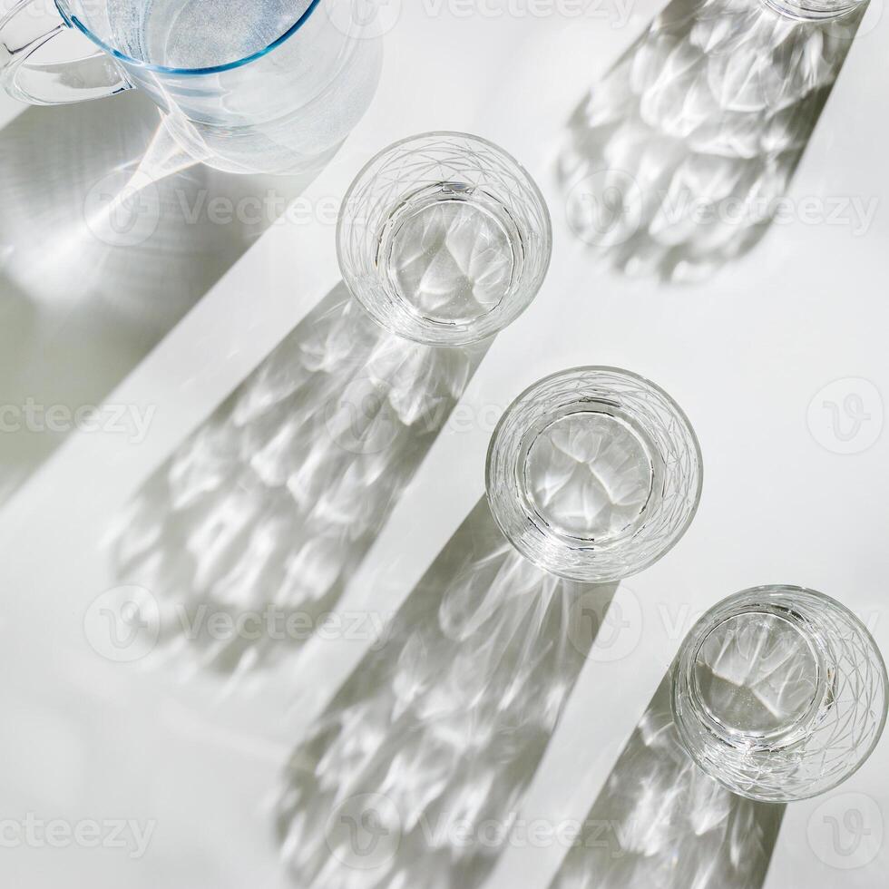Water Glass with shadows at sunlight on white, delicate green blue color, minimal aesthetic top view shiny glasses at natural light, summer drink concept, pastel gradient interplay light and shadows photo