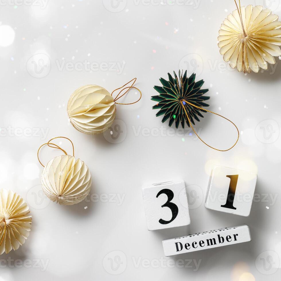 Flat lay of decorative ornaments and wood calendar date December 31st New Year's Eve, Minimal layout with paper festive decor beige balls and green Christmas Tree Ornament, honeycomb decor photo