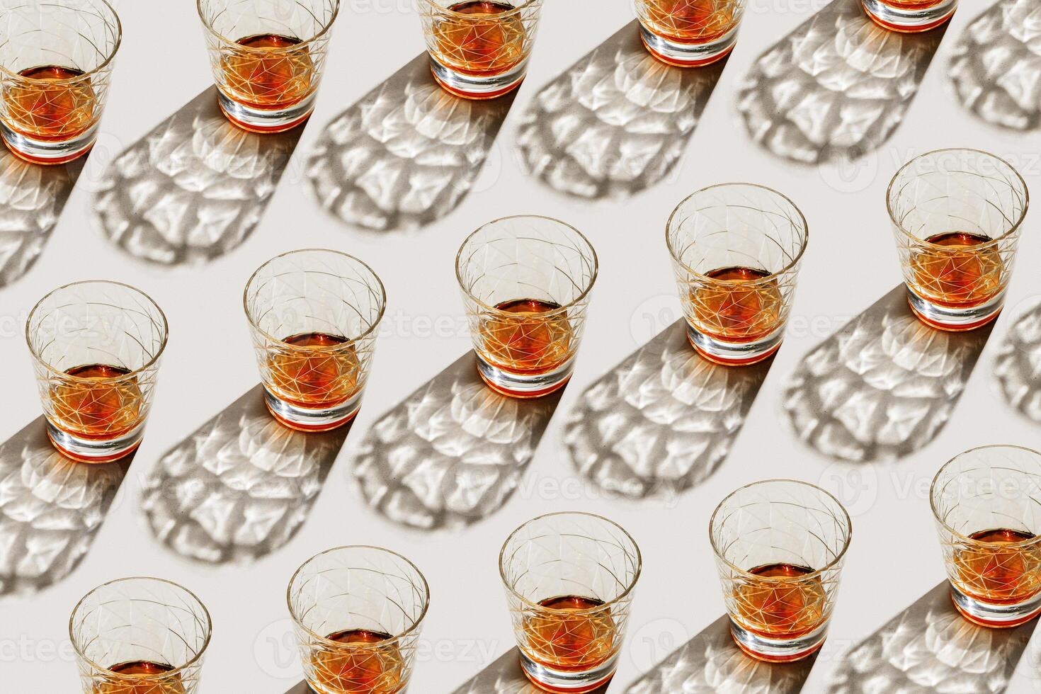 Glasses with strong drink as minimal geometric pattern, beautiful shadow at sunlight on beige textured background, aesthetic photo shiny glass, sun glare, alcohol drinks concept, summer
