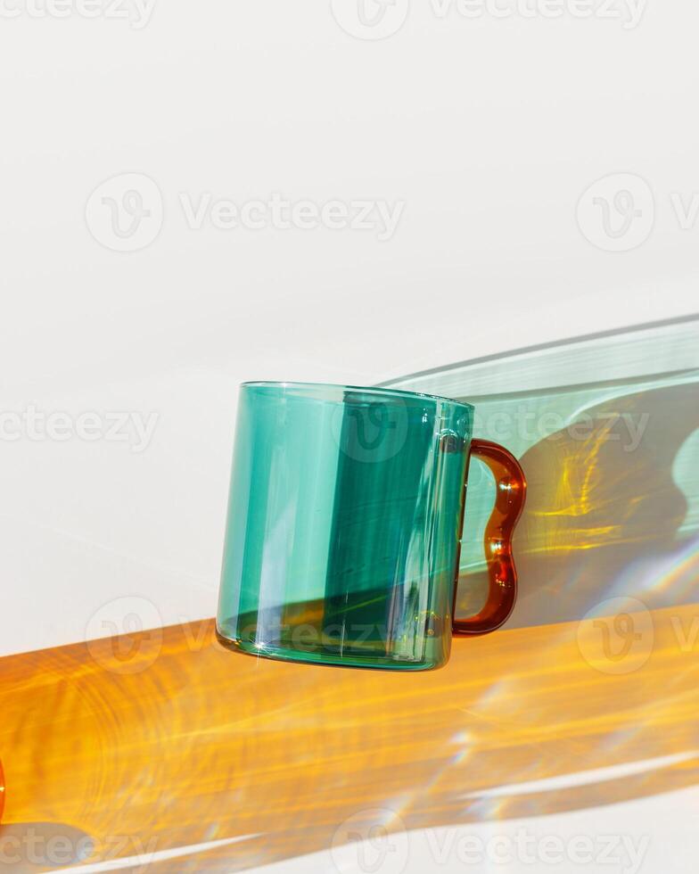 Modern Glass Cup with Vibrant sunlight Shadows, Minimal photo of transparent green colored glass mug. Golden light reflections and shadow on white background, lifestyle designs, homeware decor