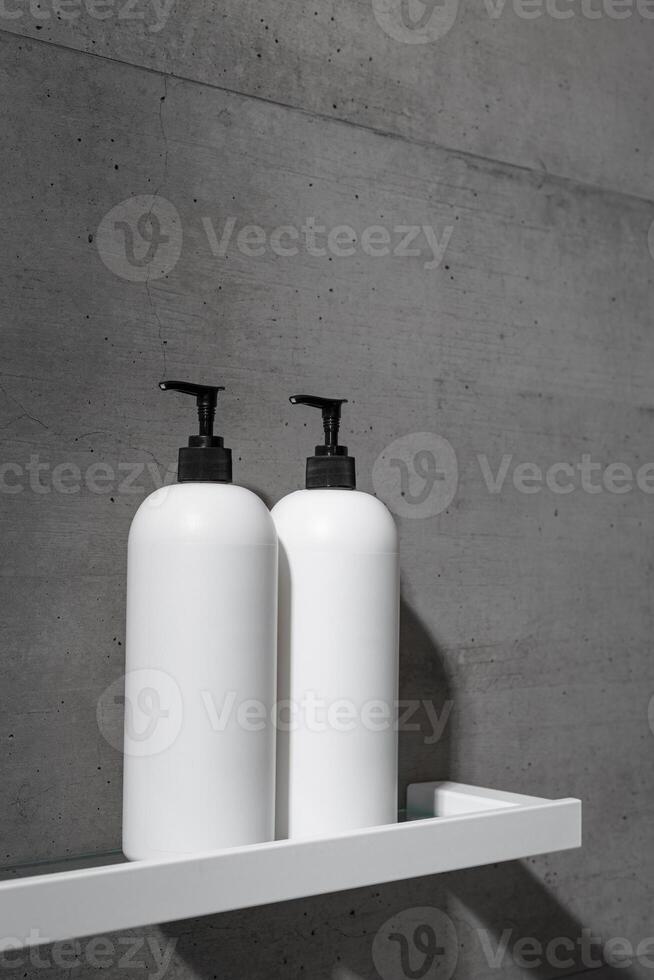 White bottles mock up on white shelf on gray concrete background, close up shampoo, conditioner. Aesthetic view beauty products in modern minimal bathroom neutral color. Side view, copyspace photo