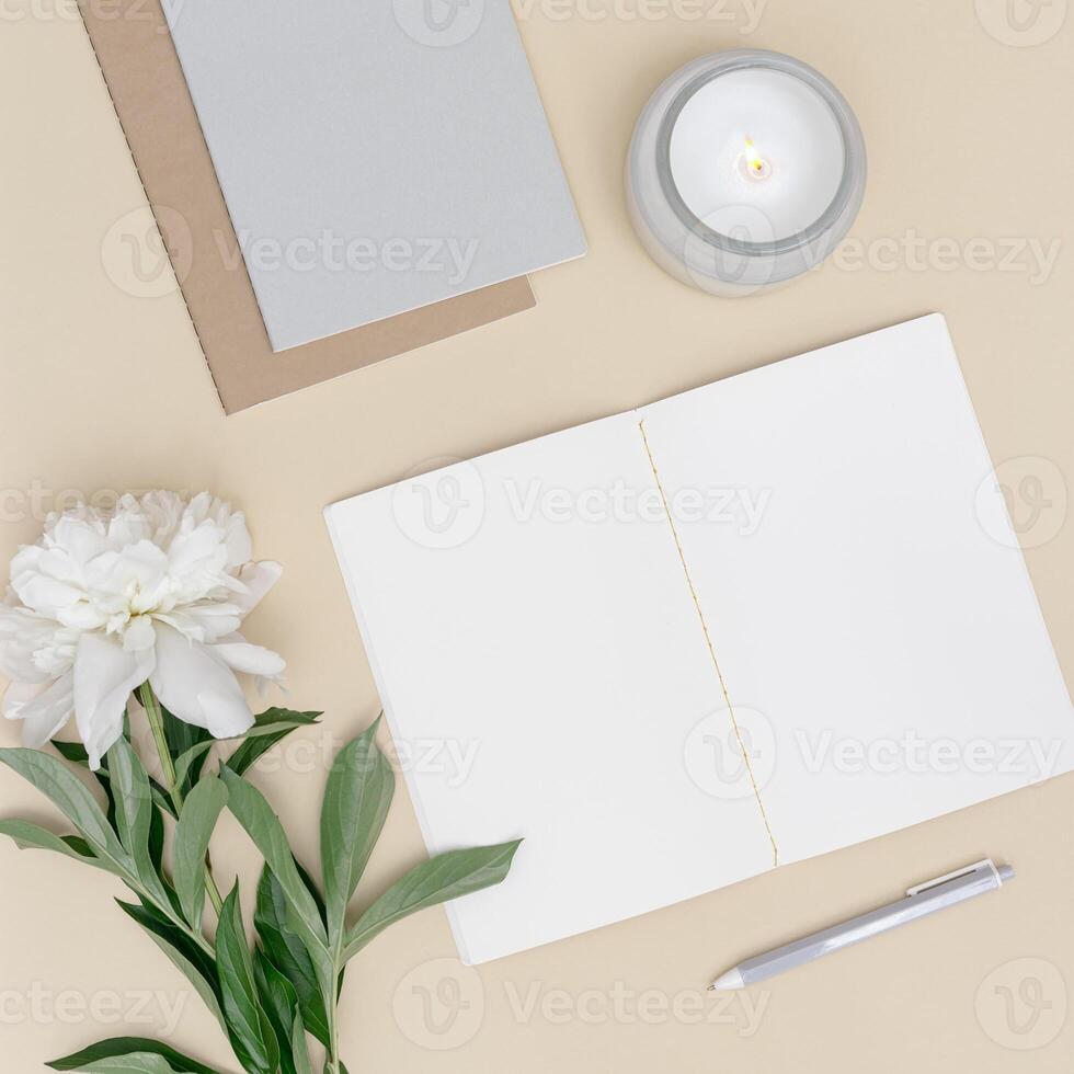 Top view office table desk. Workspace with blank copybook, pen, white peony flower with green leaf and candle photo