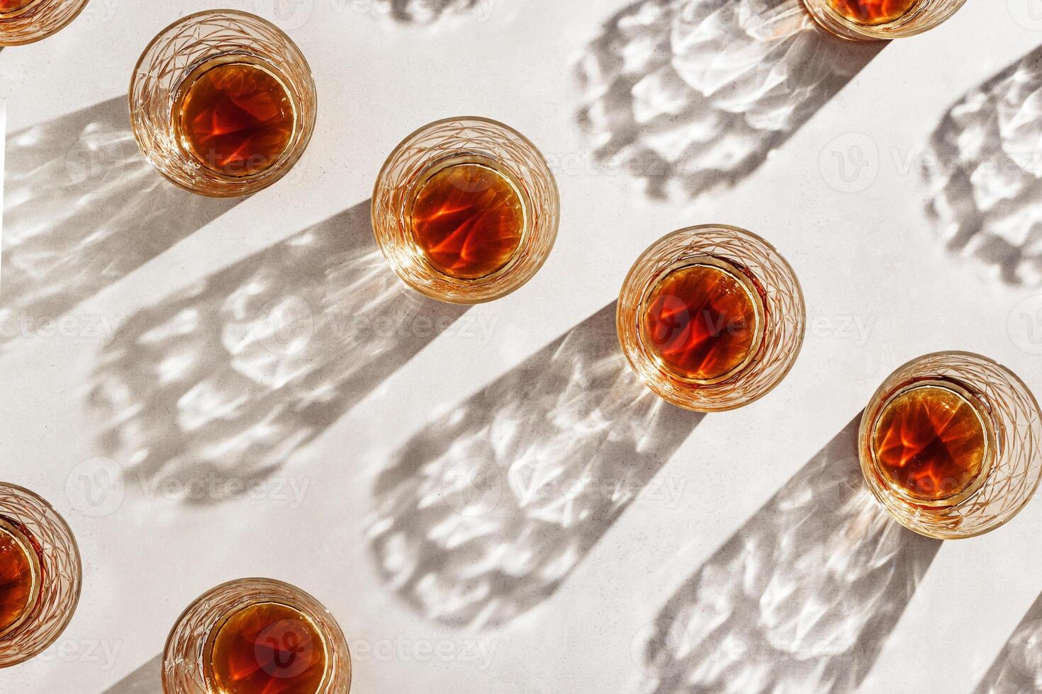 Whiskey Glasses with Shadow and sunlight Reflection on beige, glass strong alcohol, top view repeated pattern, aesthetic top view summer still life, refraction at crystal shine cups, caustics photo