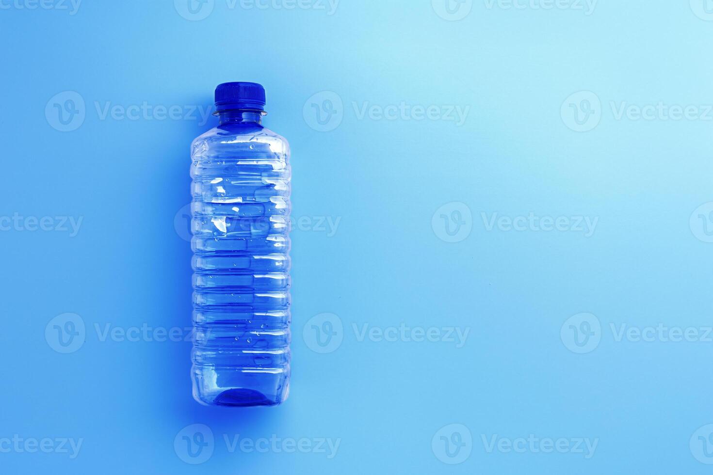 Clear plastic water bottle with blue cap on light blue background with soft shadow, copyspace. Minimal top view photo, themes of ecology, recycling, sustainable living, reduce disposable plastics photo