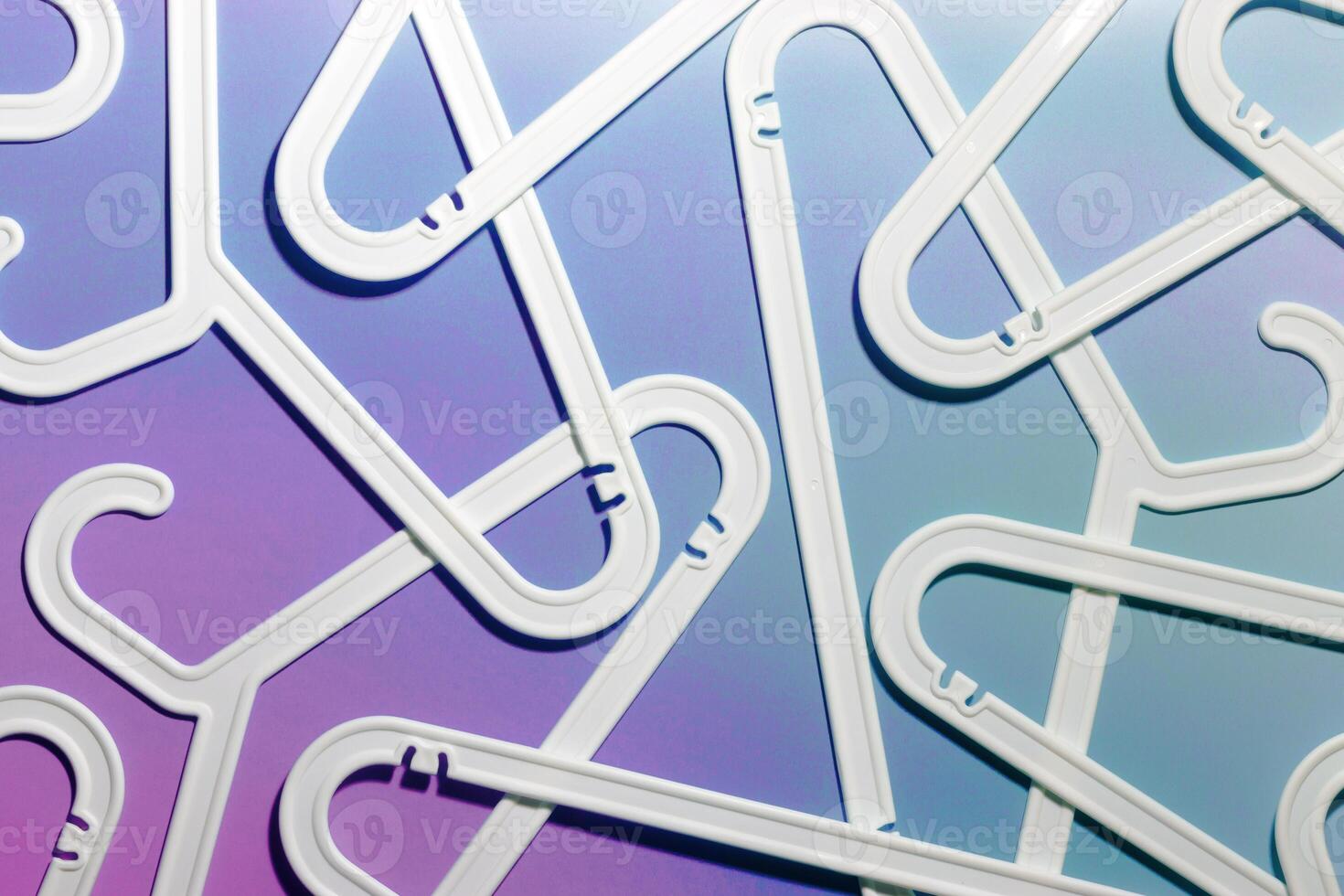White Plastic hangers as abstract minimal pattern on neon gradient background of purple and blue tint, Clothes rack for organizing clothes in closets or retail stores for hanging of garments, top view photo