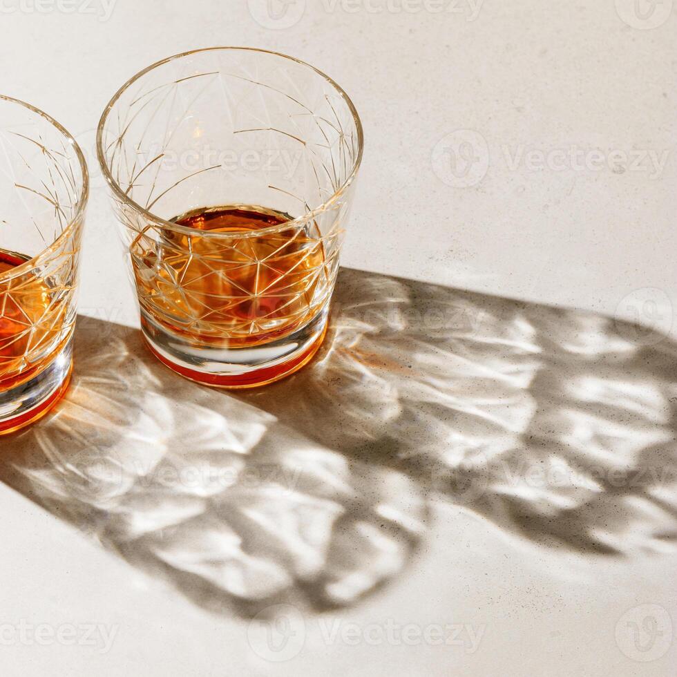 Crystal Glasses with strong drink, beautiful shadow at sunlight on beige textured background, minimal trend, aesthetic side view shiny glass, sun glare, strong alcohol drink concept, summertime, photo