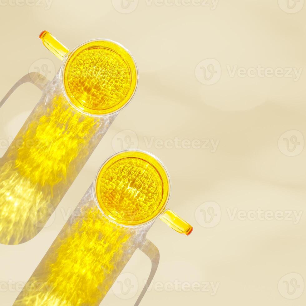 Top view of two yellow colored glass mugs creating vivid light reflections and caustics on beige background. Transparent cup at sunlight with sun glare, summer drink photo, golden tones, copyspace photo