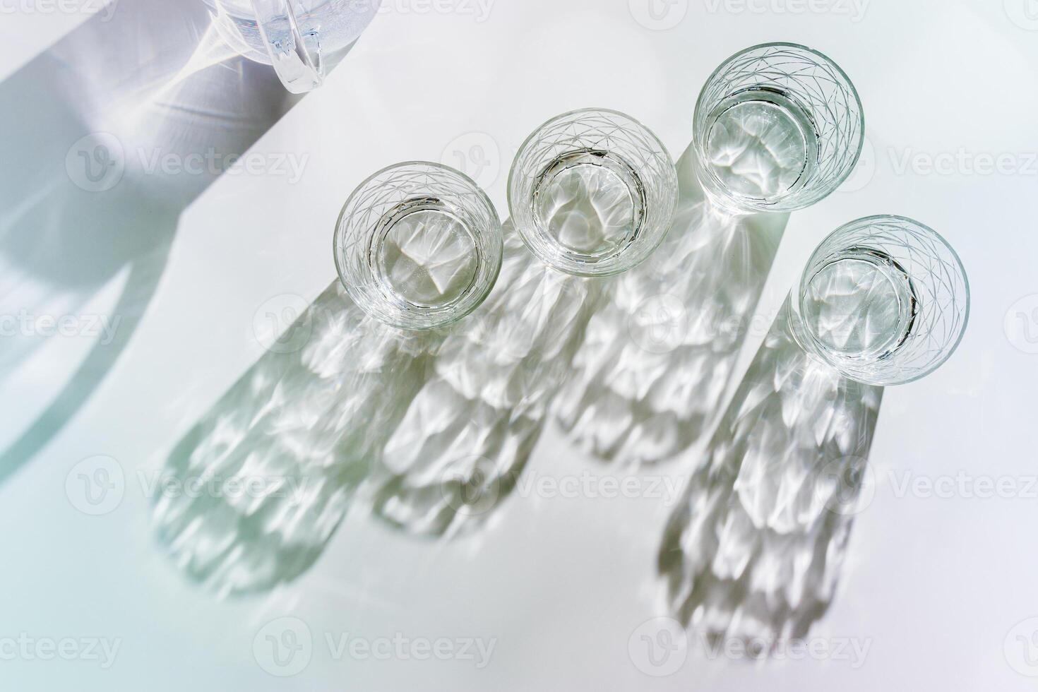 Water Glasses and water jug with Shadows and sunlight Reflection on white background, colored photo minimal style, aesthetic summer still life, refraction through crystal shine cups, caustics effect