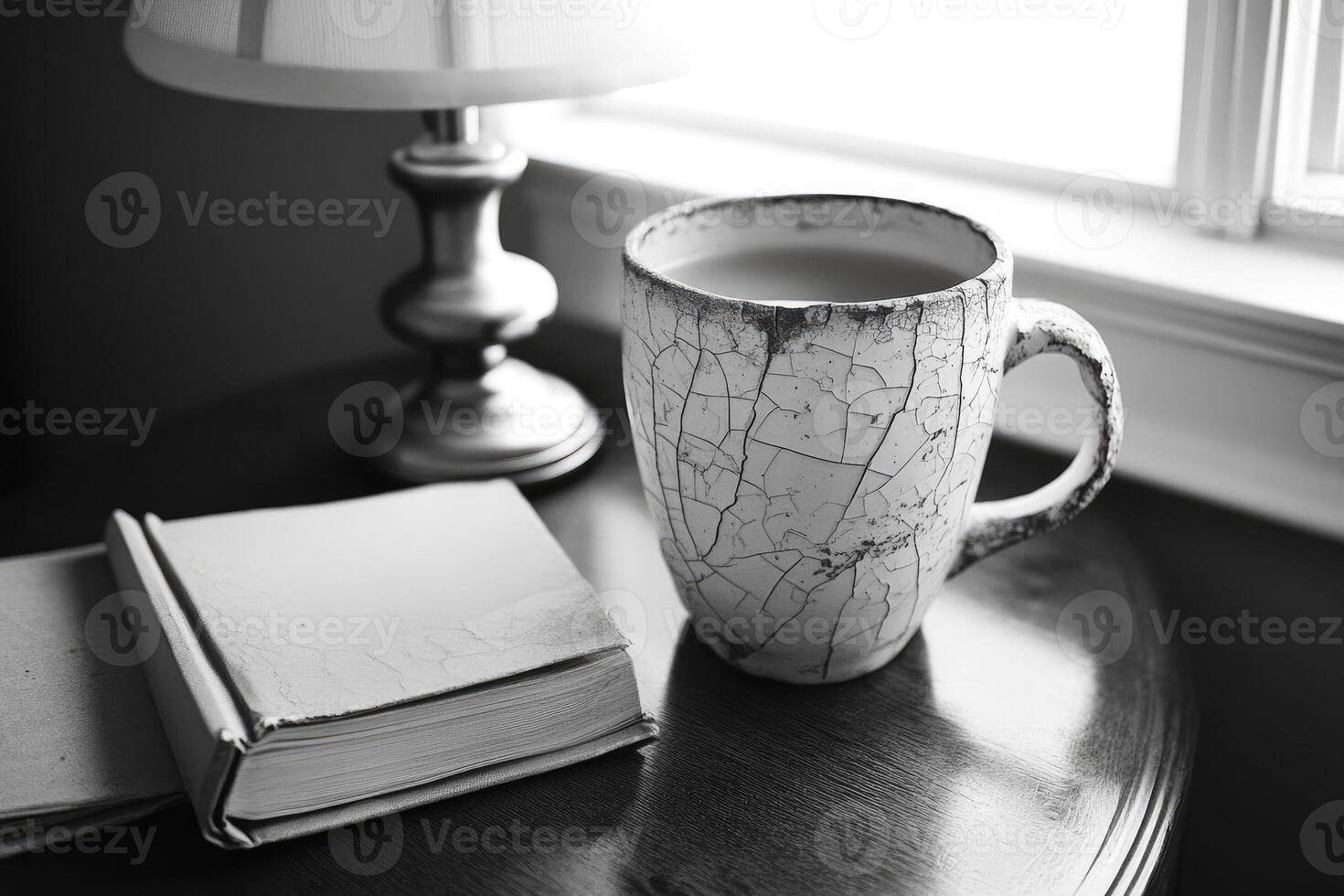 Cracked ceramic mug filled with beverage beside an open book on a wooden table near a lamp photo