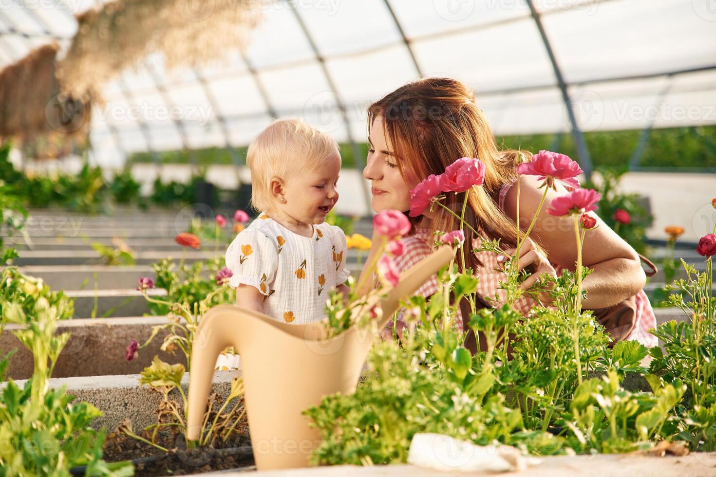 Showing red flowers to the baby. Mother and daughter are in ,,the greenhouse.. photo