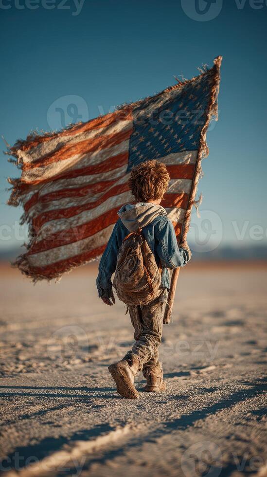 Young boy carrying worn American flag while walking across dusty landscape under clear blue sky photo