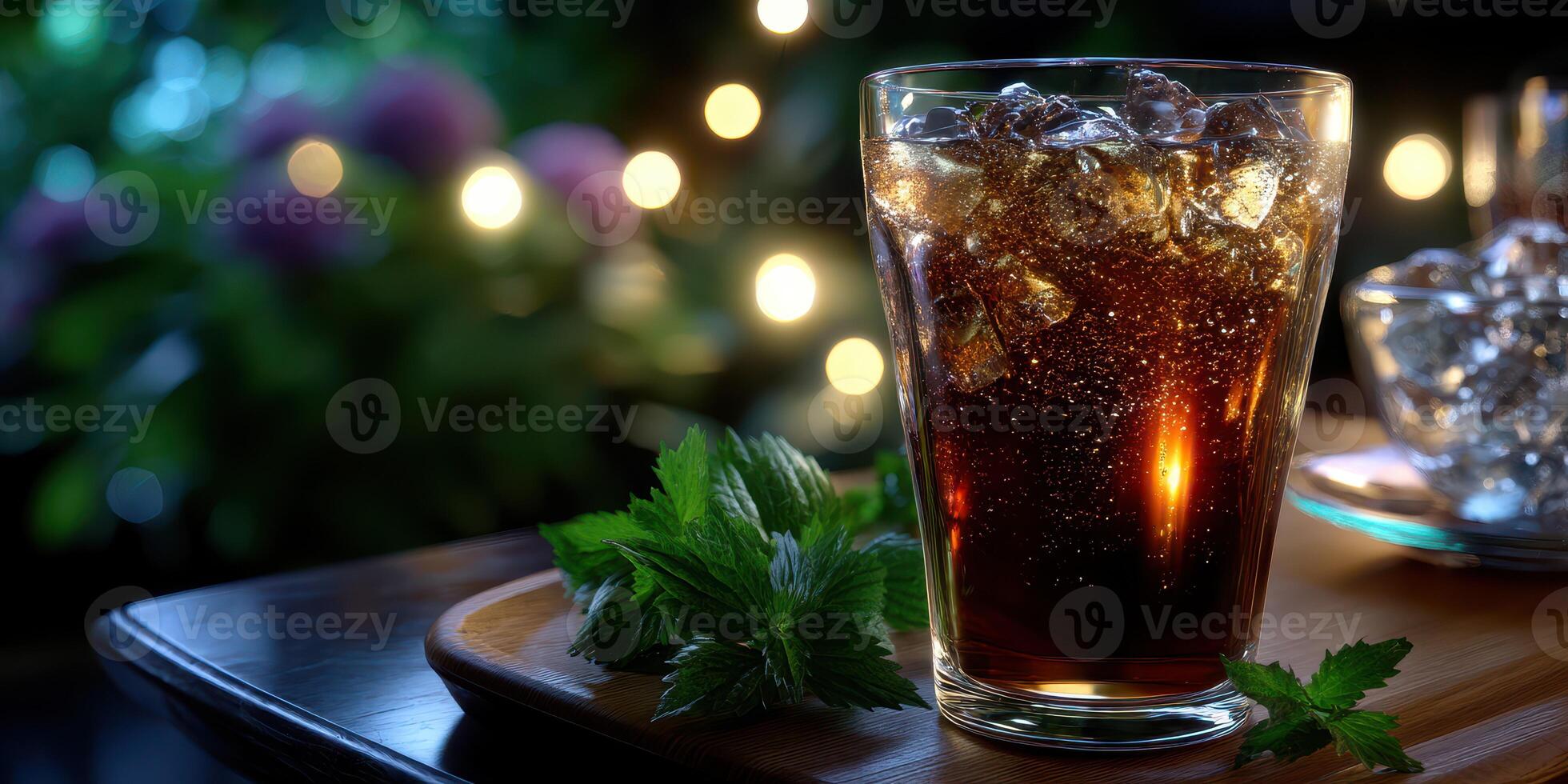 Refreshing beverage with ice in a glass placed on a wooden table surrounded by greenery and soft lighting during the evening photo