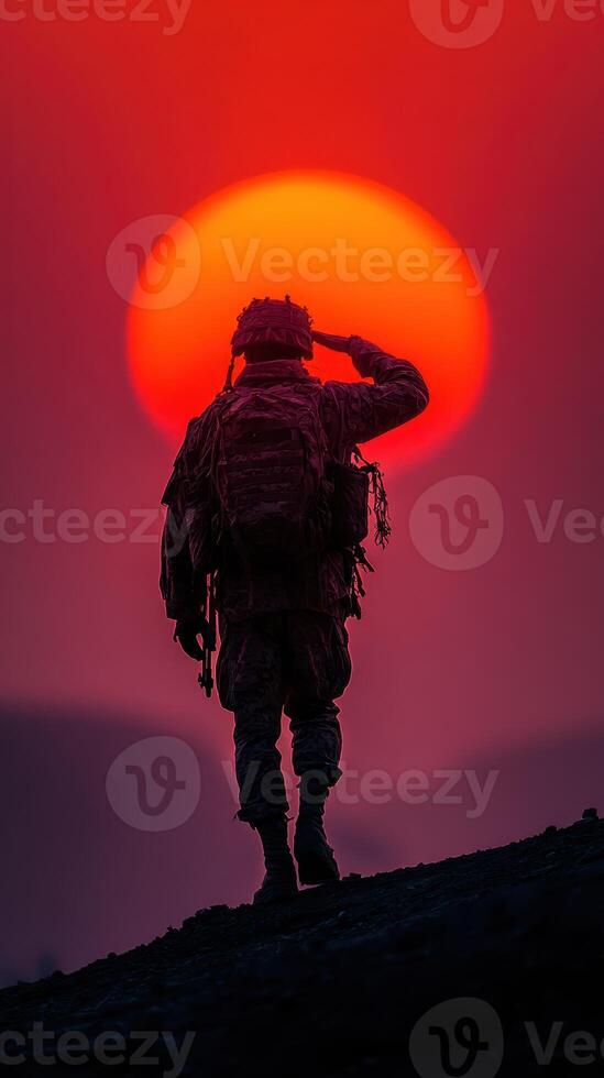 Soldier saluting the sunset with a warm red backdrop overlooking a mountainous landscape photo