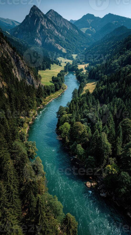 Serene river winding through lush green valley surrounded by majestic mountains on a clear sunny day photo