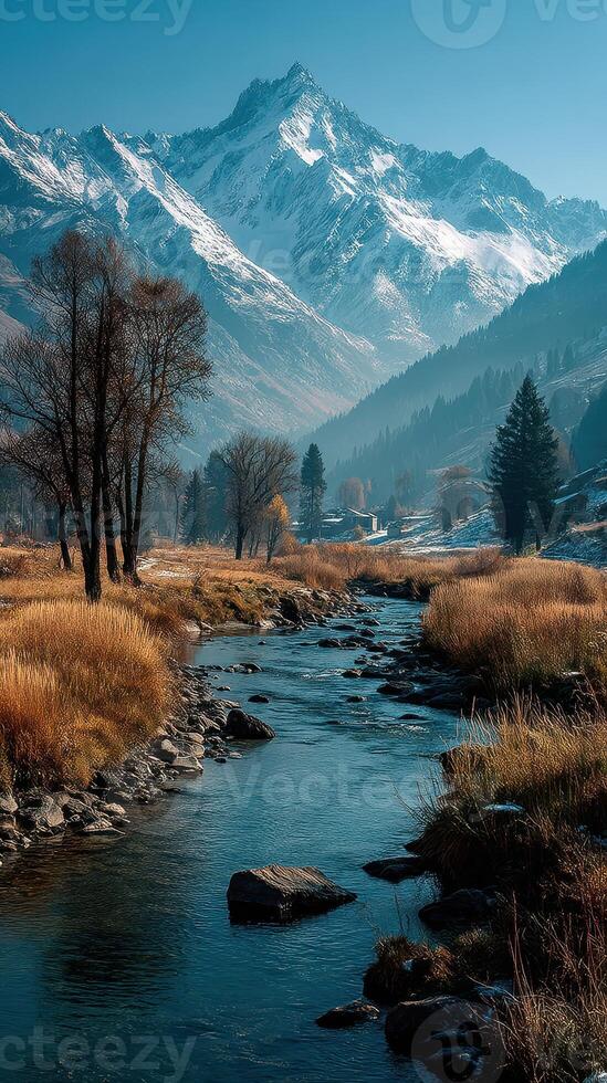 Majestic mountain landscape with a tranquil river flowing through golden grass and snow-capped peaks photo