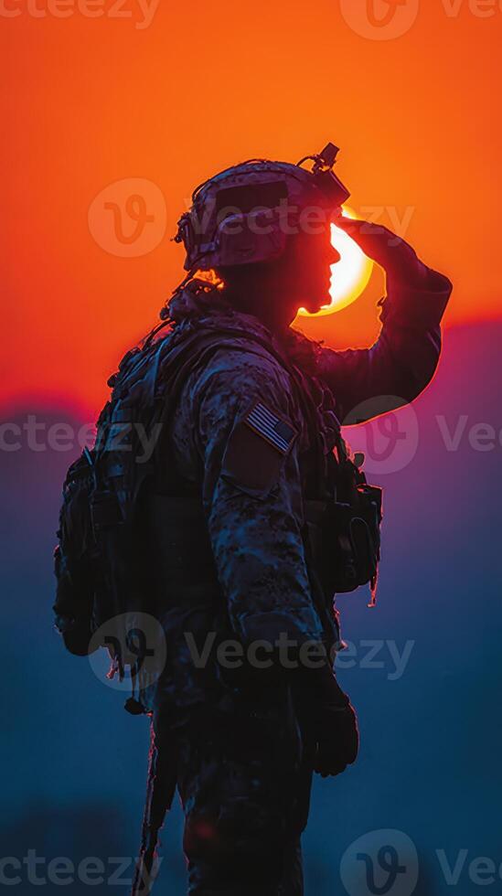 Soldier silhouetted against a vibrant sunset while saluting in a mountainous environment photo