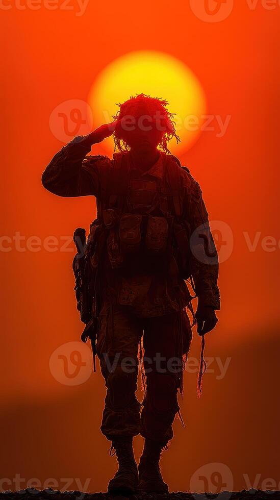 Soldier salutes the setting sun in a dramatic silhouette against a vibrant orange sky photo