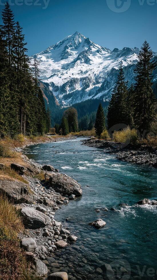 Snow-capped mountain peaks reflect in a clear river surrounded by evergreen trees in a serene landscape photo