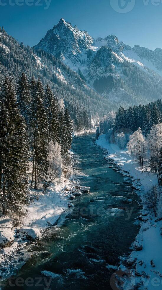Serene winter landscape with a flowing river and majestic mountains in the background during a clear daytime in a forested area photo