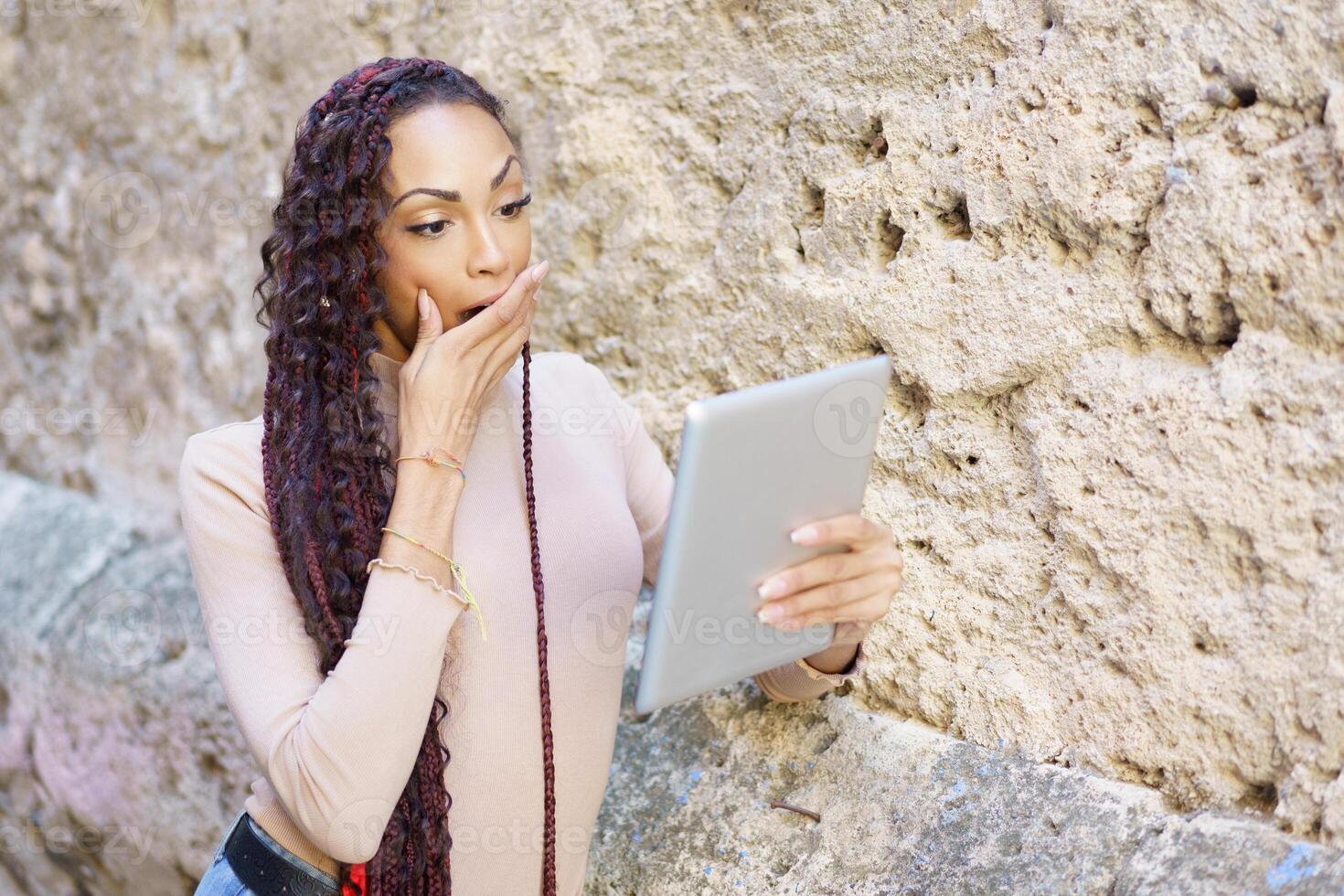 A surprised woman is looking intently at a tablet while in a bustling urban setting photo