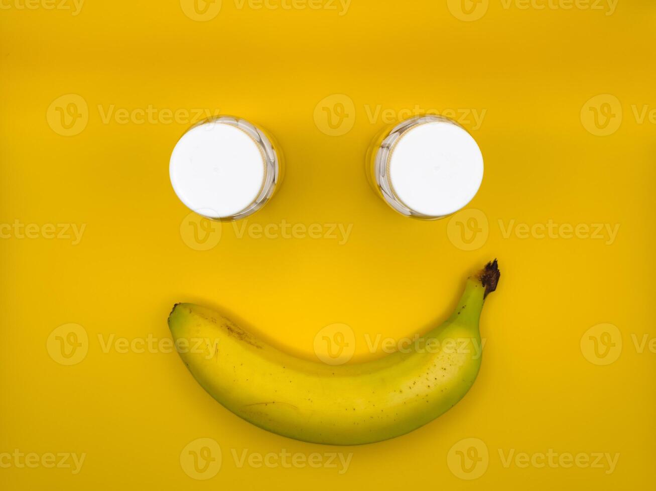 Smiley face made of one banana and two medicine bottles in the center of the image, top view photo