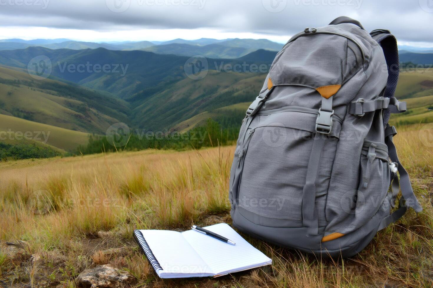 Backpack and notebook resting on mountain meadow overlooking scenic valley photo