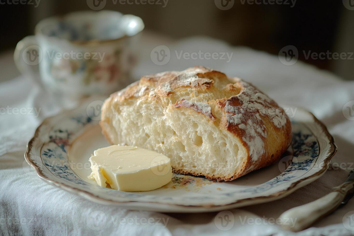 Crusty bread loaf with butter and teacup on tablecloth photo
